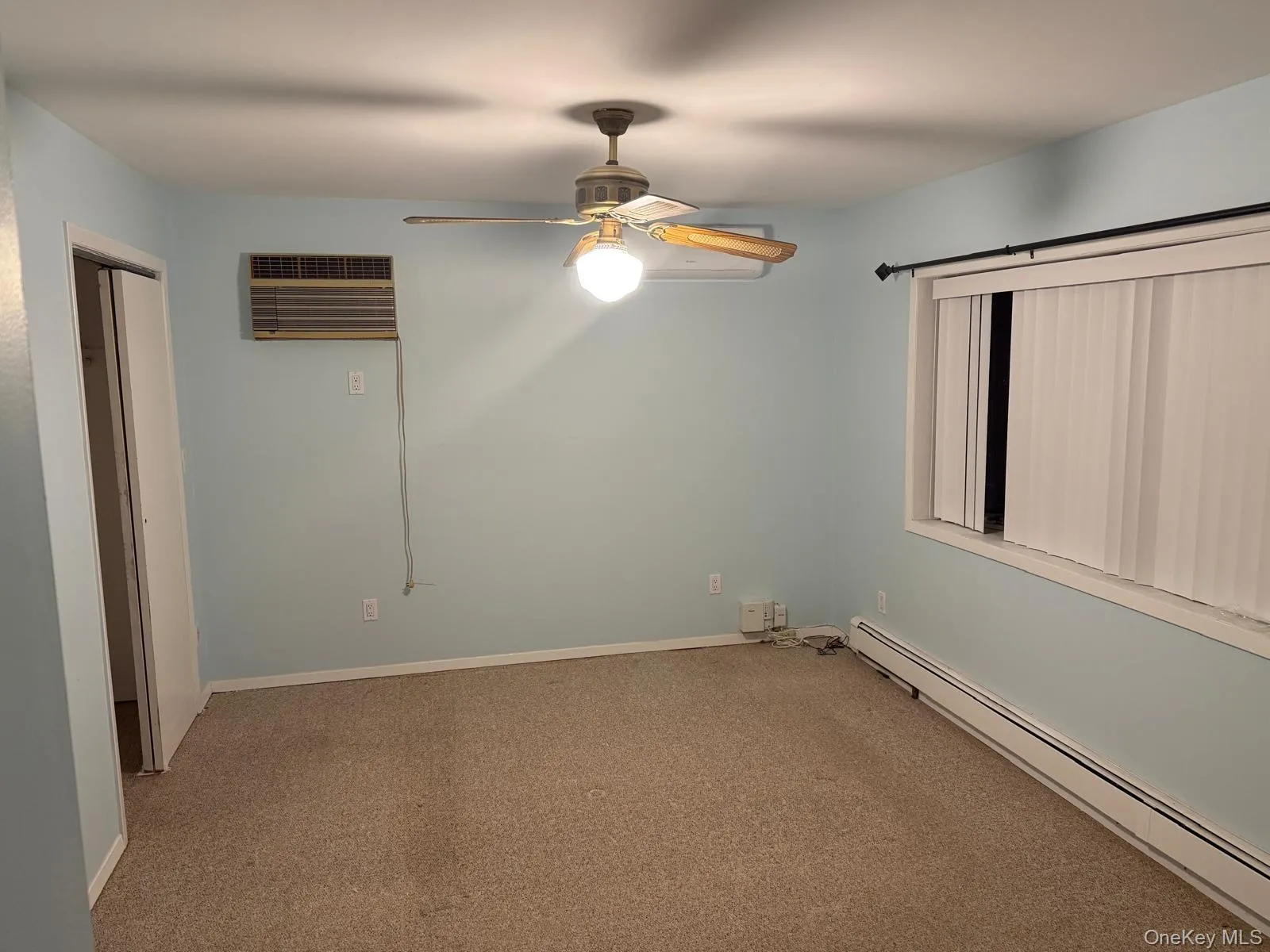 Carpeted empty room featuring baseboard heating, ceiling fan, and a wall unit AC Carpeted empty room featuring baseboard heating, ceiling fan, and a wall unit AC