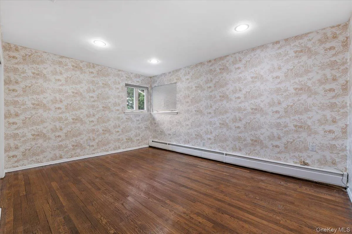 Empty room featuring baseboard heating, dark wood-style floors, wallpapered walls, and recessed lighting Empty room featuring baseboard heating, dark wood-style floors, wallpapered walls, and recessed lighting