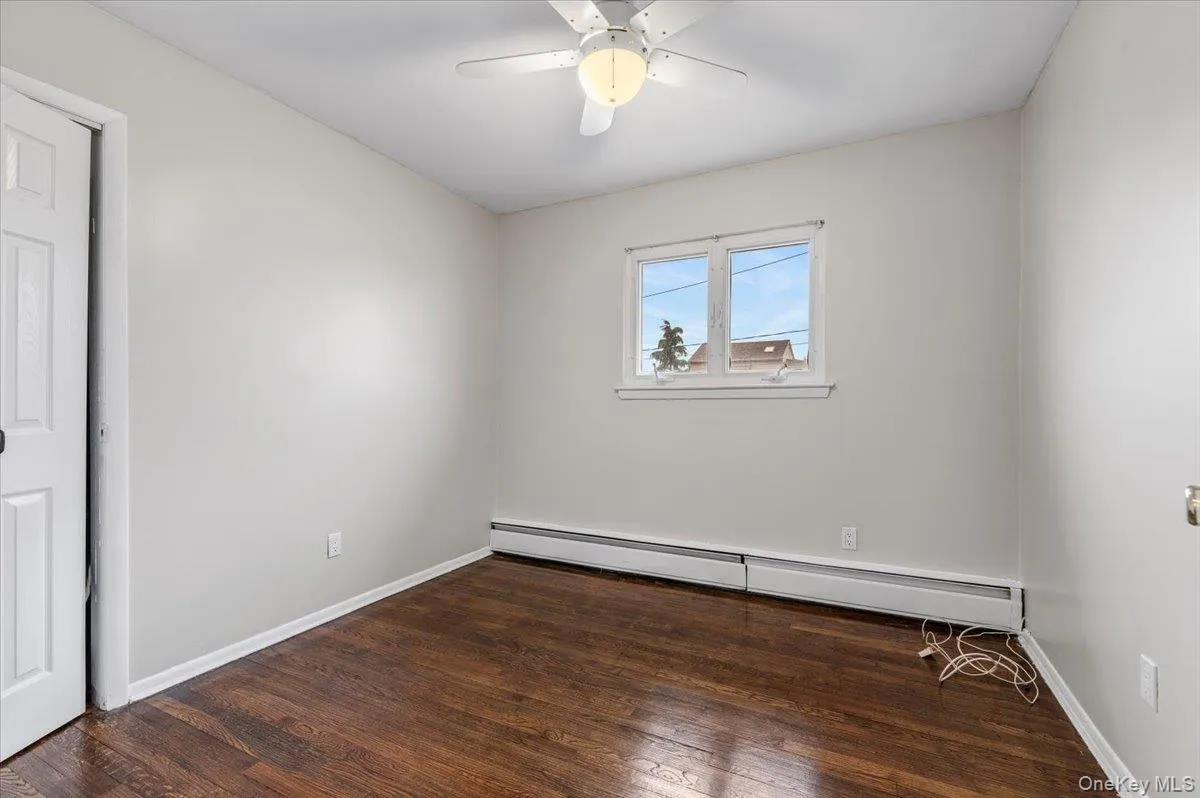 Unfurnished room featuring dark wood-style floors, baseboard heating, and ceiling fan Unfurnished room featuring dark wood-style floors, baseboard heating, and ceiling fan