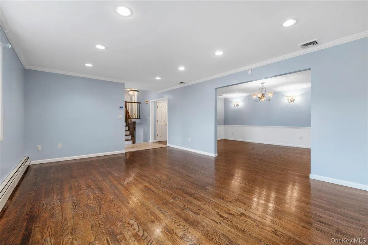 Unfurnished living room featuring recessed lighting, baseboard heating, dark wood-style floors, stairs, and ornamental molding Unfurnished living room featuring recessed lighting, baseboard heating, dark wood-style floors, stairs, and ornamental molding