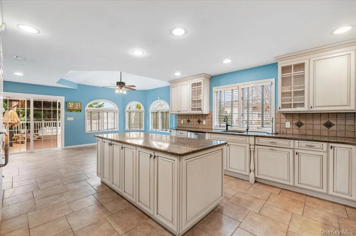 Kitchen featuring cream cabinetry, decorative backsplash, dark stone countertops, glass insert cabinets, and recessed lighting Kitchen featuring cream cabinetry, decorative backsplash, dark stone countertops, glass insert cabinets, and recessed lighting