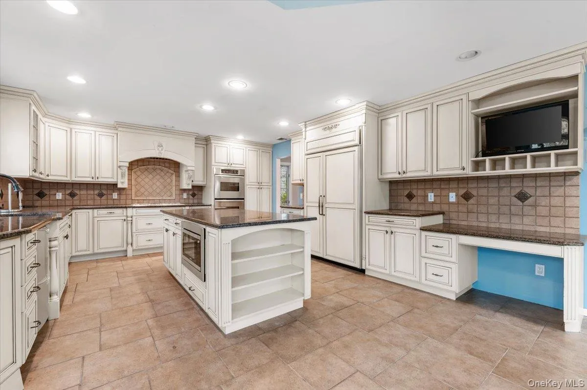Kitchen with open shelves, dark stone counters, built in appliances, a kitchen island, and tasteful backsplash Kitchen with open shelves, dark stone counters, built in appliances, a kitchen island, and tasteful backsplash