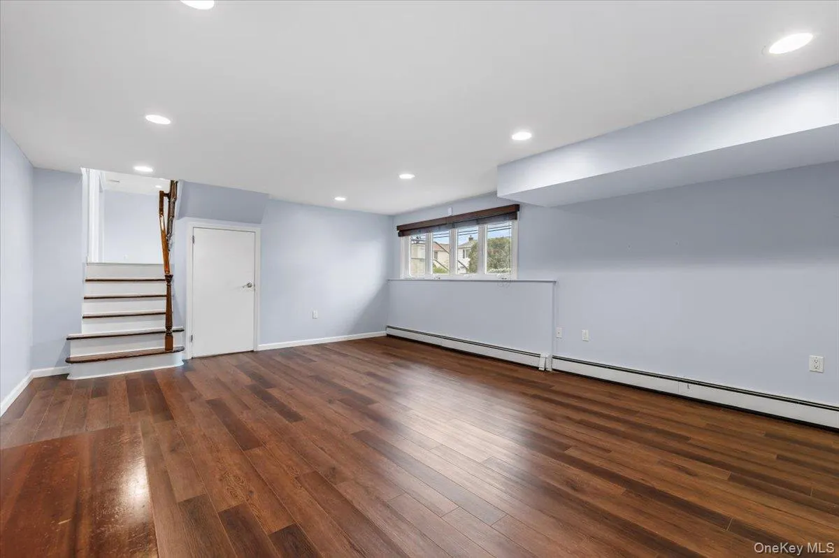 Basement with dark wood-style flooring, stairway, recessed lighting, and baseboard heating Basement with dark wood-style flooring, stairway, recessed lighting, and baseboard heating
