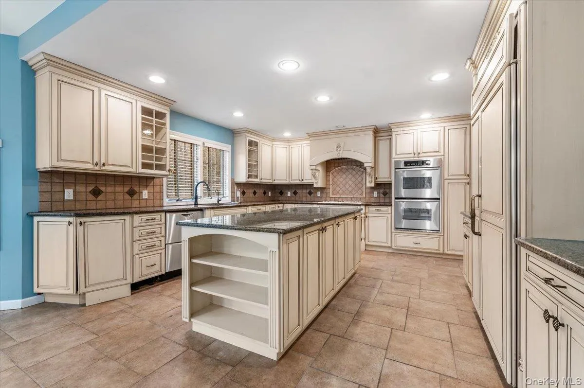Kitchen with cream cabinetry, dark stone countertops, open shelves, appliances with stainless steel finishes, and glass insert cabinets Kitchen with cream cabinetry, dark stone countertops, open shelves, appliances with stainless steel finishes, and glass insert cabinets