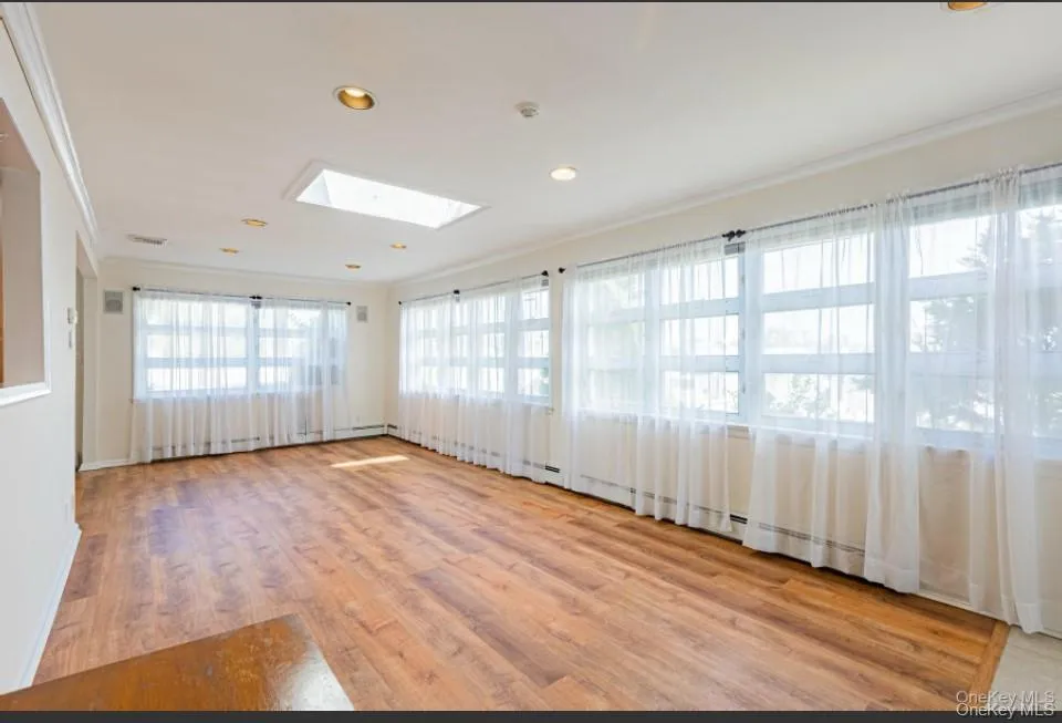 Unfurnished room featuring crown molding, light wood-style floors, a skylight, recessed lighting, and a baseboard heating unit Unfurnished room featuring crown molding, light wood-style floors, a skylight, recessed lighting, and a baseboard heating unit