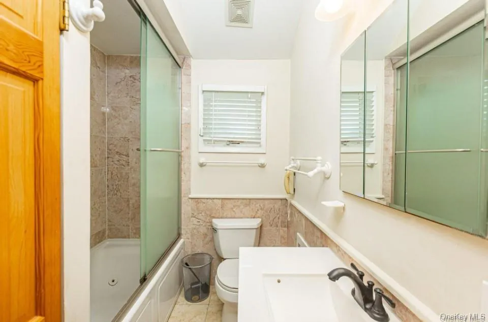 Full bathroom featuring tile walls, wainscoting, vanity, and enclosed tub / shower combo Full bathroom featuring tile walls, wainscoting, vanity, and enclosed tub / shower combo