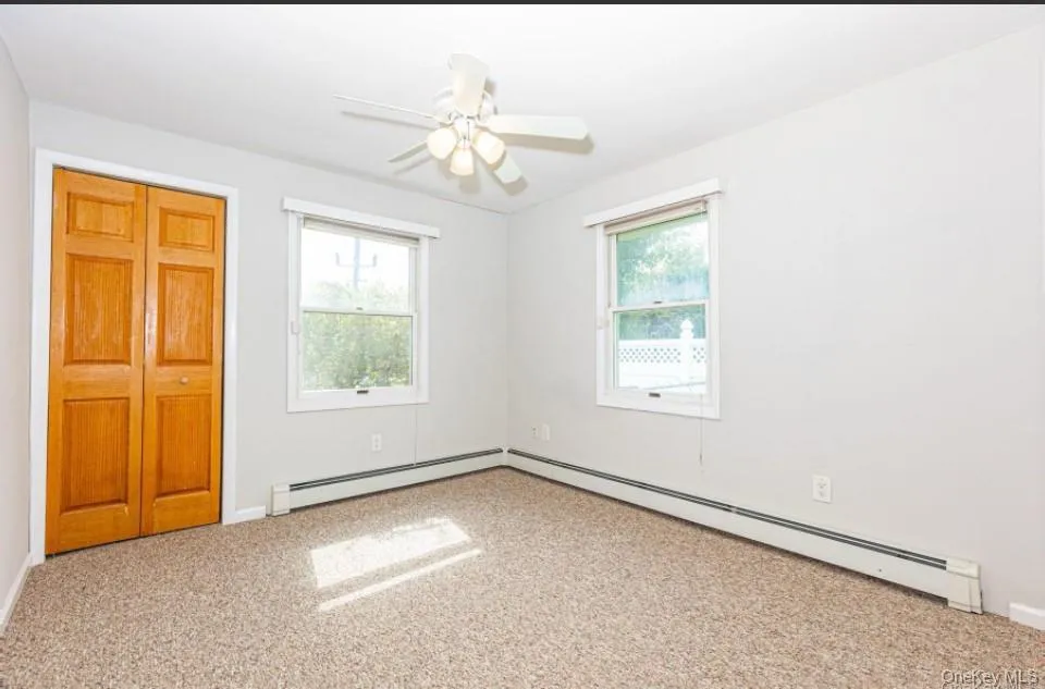 Unfurnished bedroom featuring carpet, a baseboard heating unit, and multiple windows Unfurnished bedroom featuring carpet, a baseboard heating unit, and multiple windows