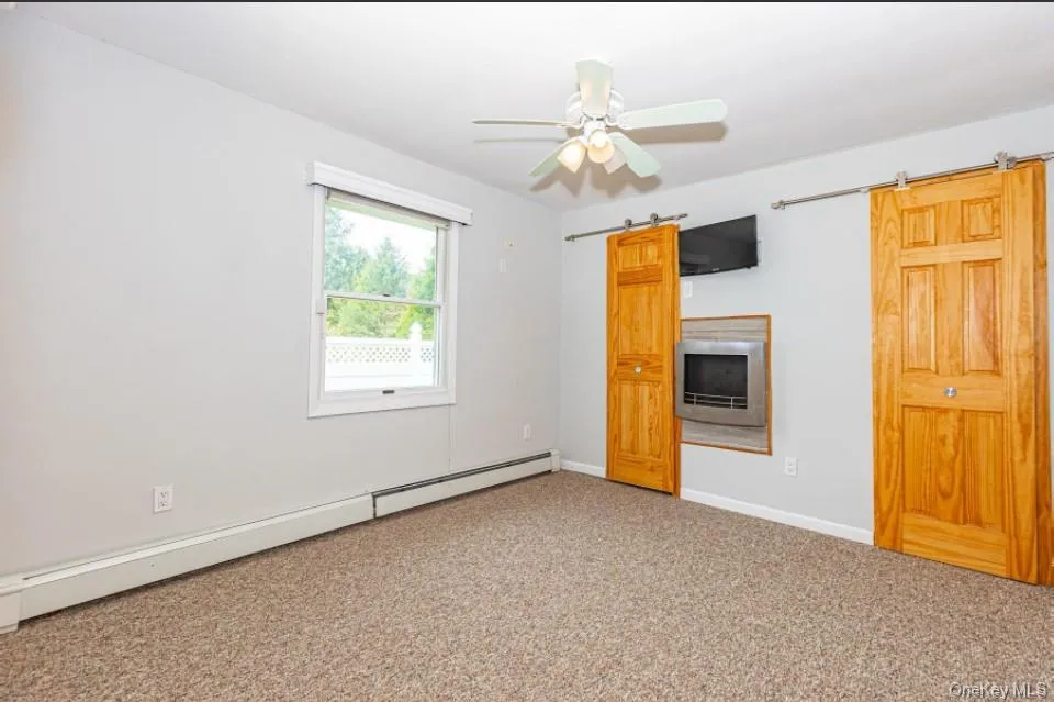 Empty room with a baseboard radiator, carpet floors, a barn door, and a ceiling fan Empty room with a baseboard radiator, carpet floors, a barn door, and a ceiling fan