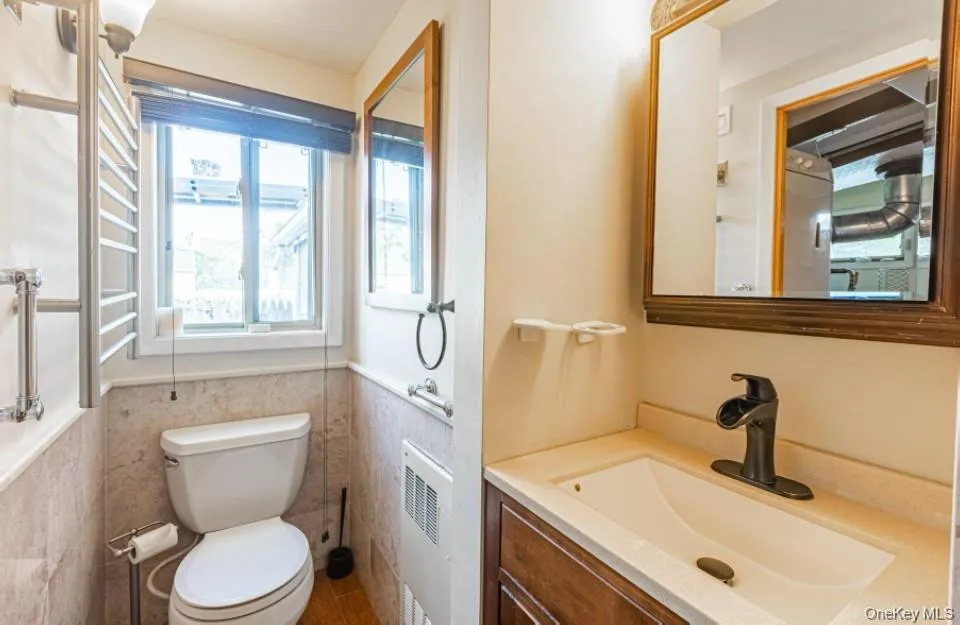 Bathroom with vanity, healthy amount of natural light, radiator, wainscoting, and tile walls Bathroom with vanity, healthy amount of natural light, radiator, wainscoting, and tile walls