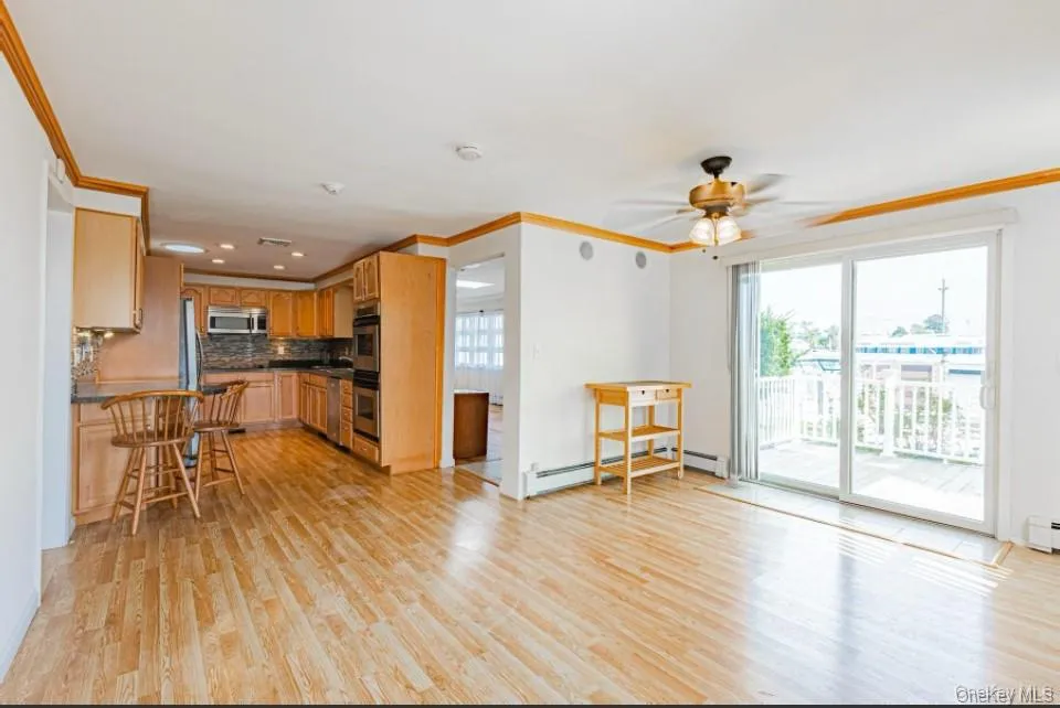 Kitchen featuring crown molding, light wood-type flooring, dark countertops, a baseboard heating unit, and backsplash Kitchen featuring crown molding, light wood-type flooring, dark countertops, a baseboard heating unit, and backsplash