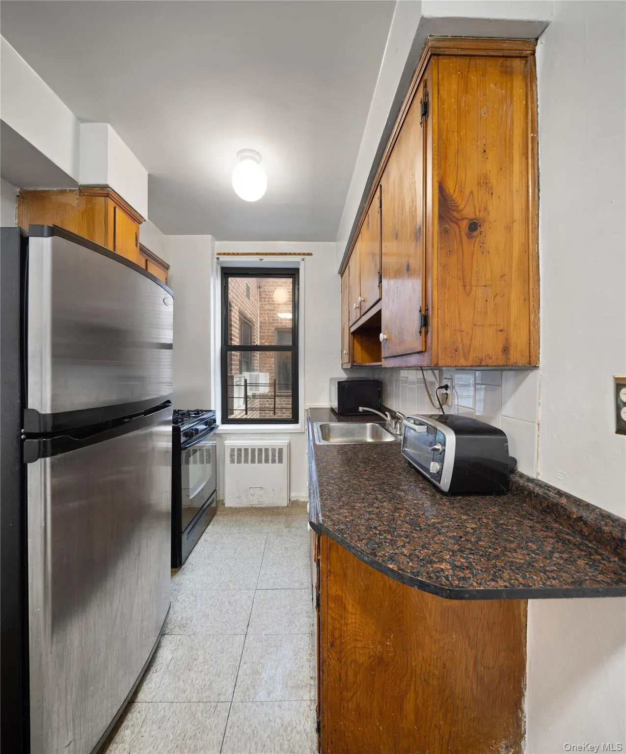 Kitchen featuring black appliances, brown cabinets, radiator, and tasteful backsplash Kitchen featuring black appliances, brown cabinets, radiator, and tasteful backsplash