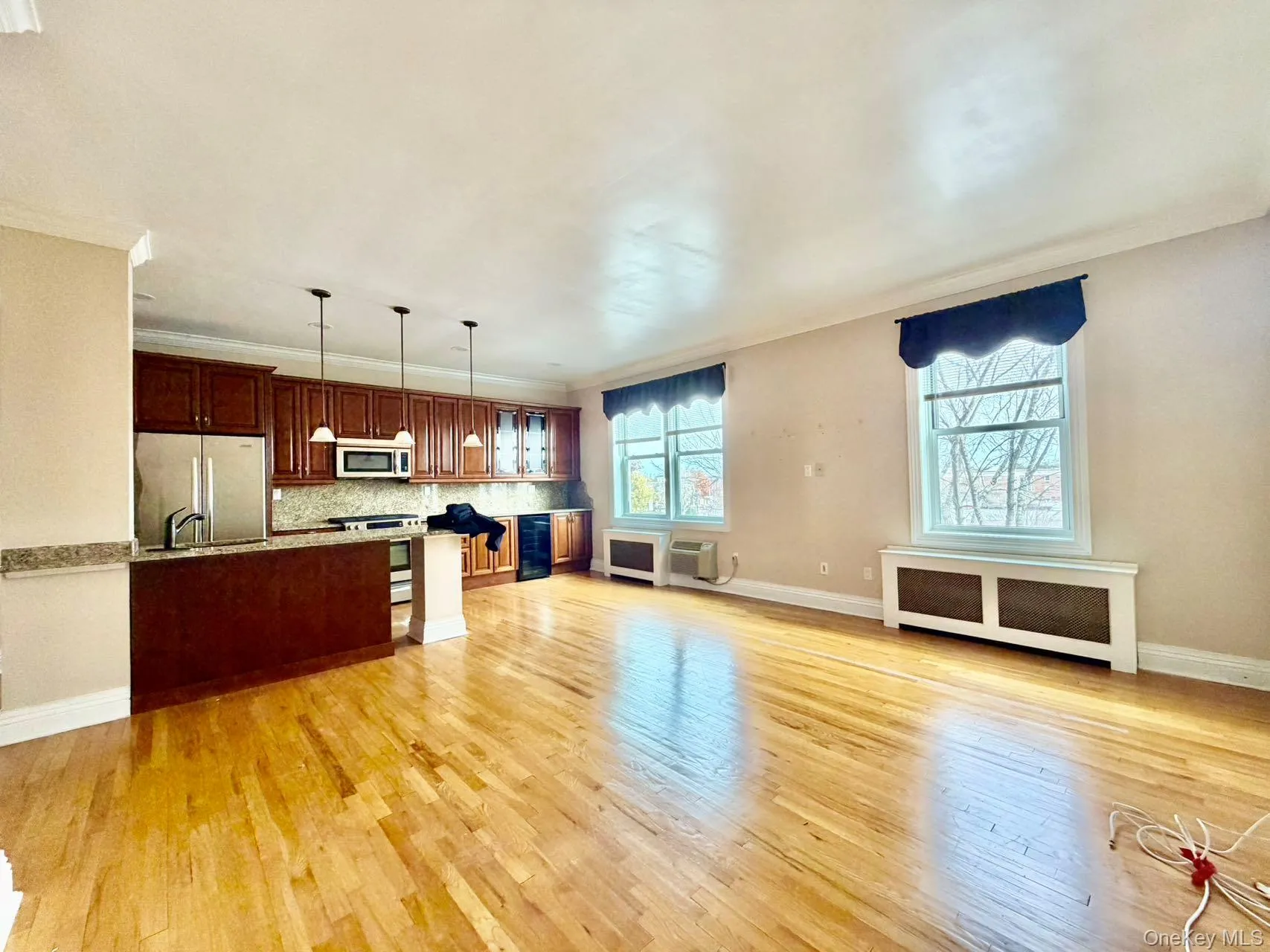 Kitchen with radiator, hanging light fixtures, open floor plan, light wood-style flooring, and crown molding Kitchen with radiator, hanging light fixtures, open floor plan, light wood-style flooring, and crown molding