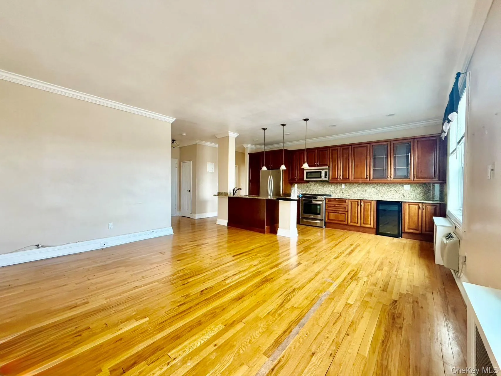 Kitchen with open floor plan, hanging light fixtures, appliances with stainless steel finishes, ornamental molding, and light wood finished floors Kitchen with open floor plan, hanging light fixtures, appliances with stainless steel finishes, ornamental molding, and light wood finished floors