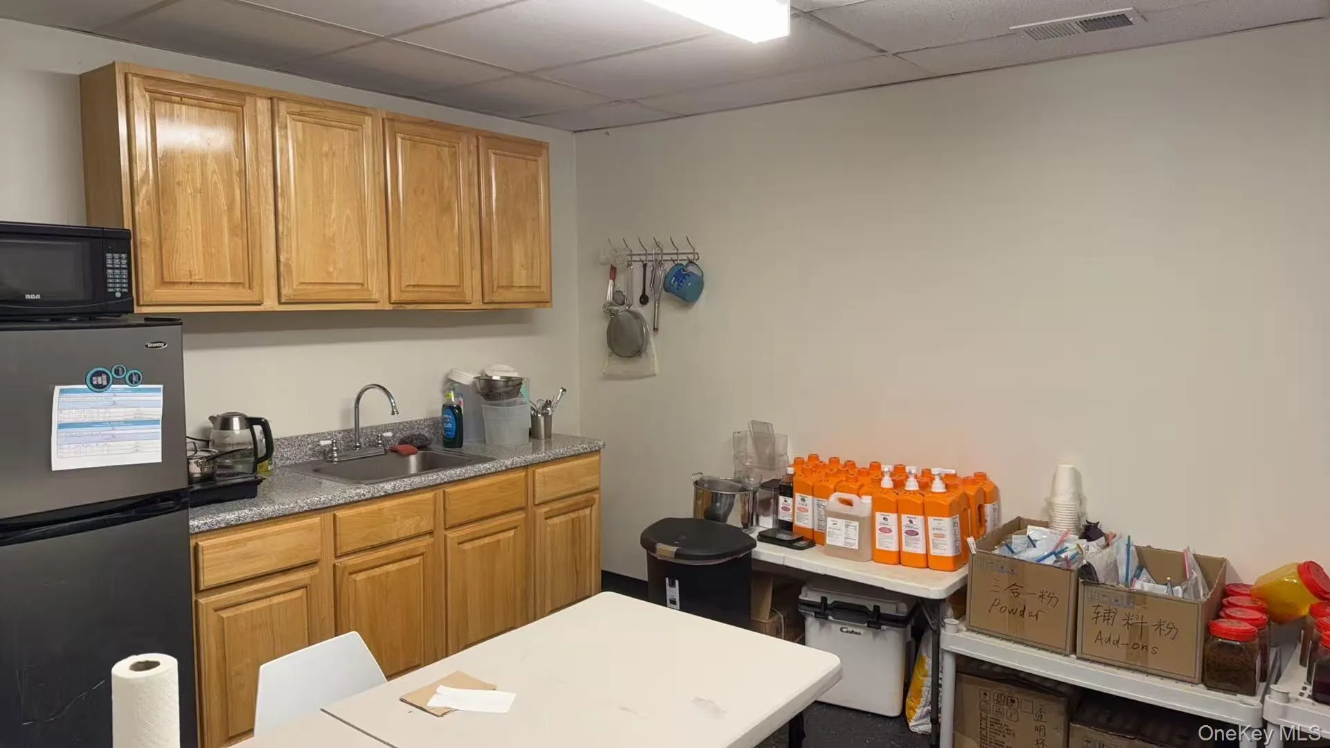 Kitchen featuring freestanding refrigerator, black microwave, and a drop ceiling Kitchen featuring freestanding refrigerator, black microwave, and a drop ceiling