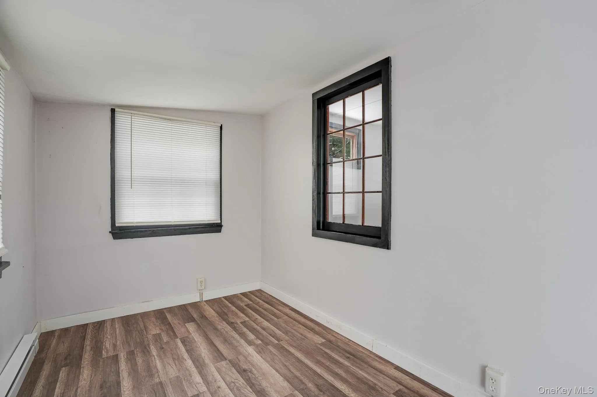 Empty room featuring wood finished floors and a baseboard heating unit Empty room featuring wood finished floors and a baseboard heating unit
