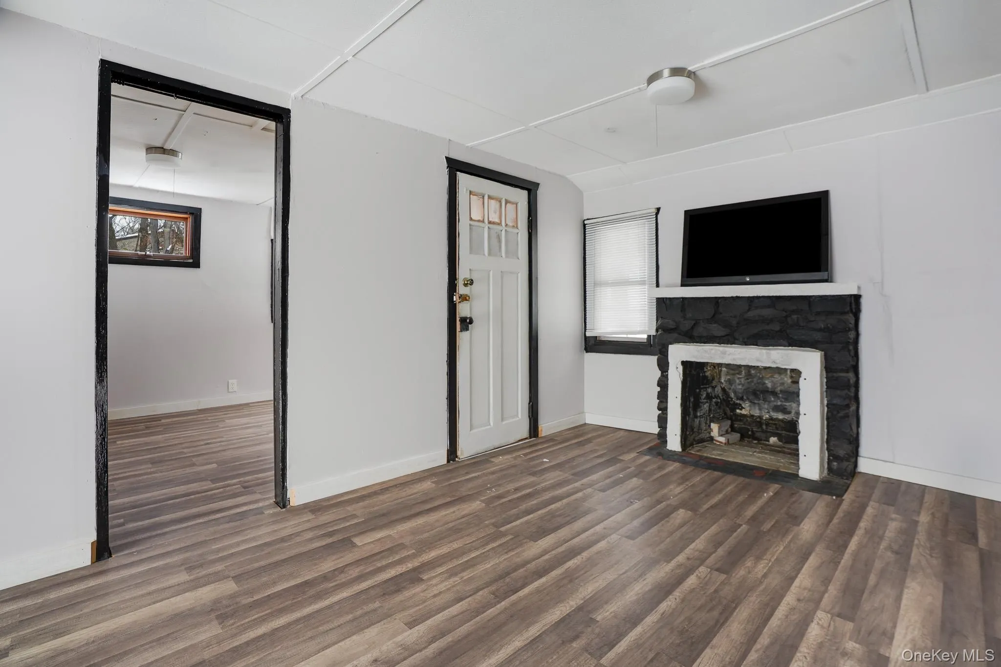 Unfurnished living room with a stone fireplace and dark wood-type flooring Unfurnished living room with a stone fireplace and dark wood-type flooring