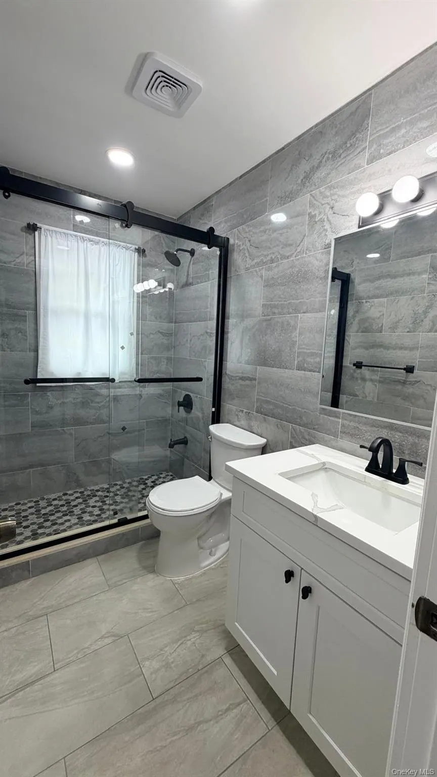 Full bathroom featuring vanity, a stall shower, light marble finish floors, and tile walls Full bathroom featuring vanity, a stall shower, light marble finish floors, and tile walls