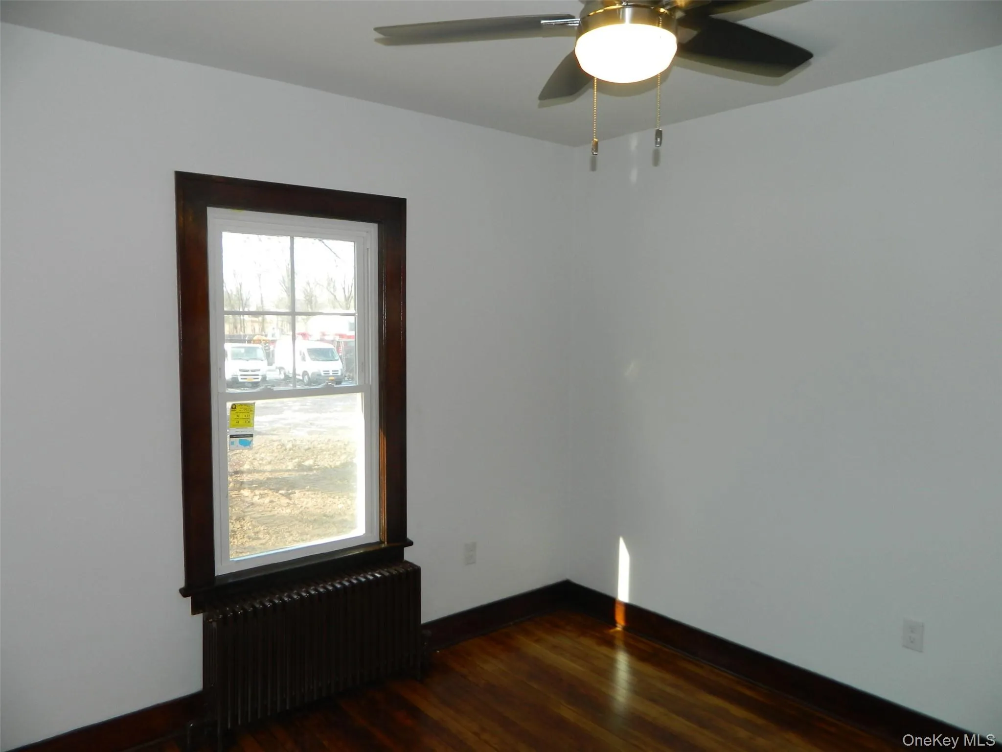 Spare room featuring radiator, dark wood-style floors, and ceiling fan Spare room featuring radiator, dark wood-style floors, and ceiling fan