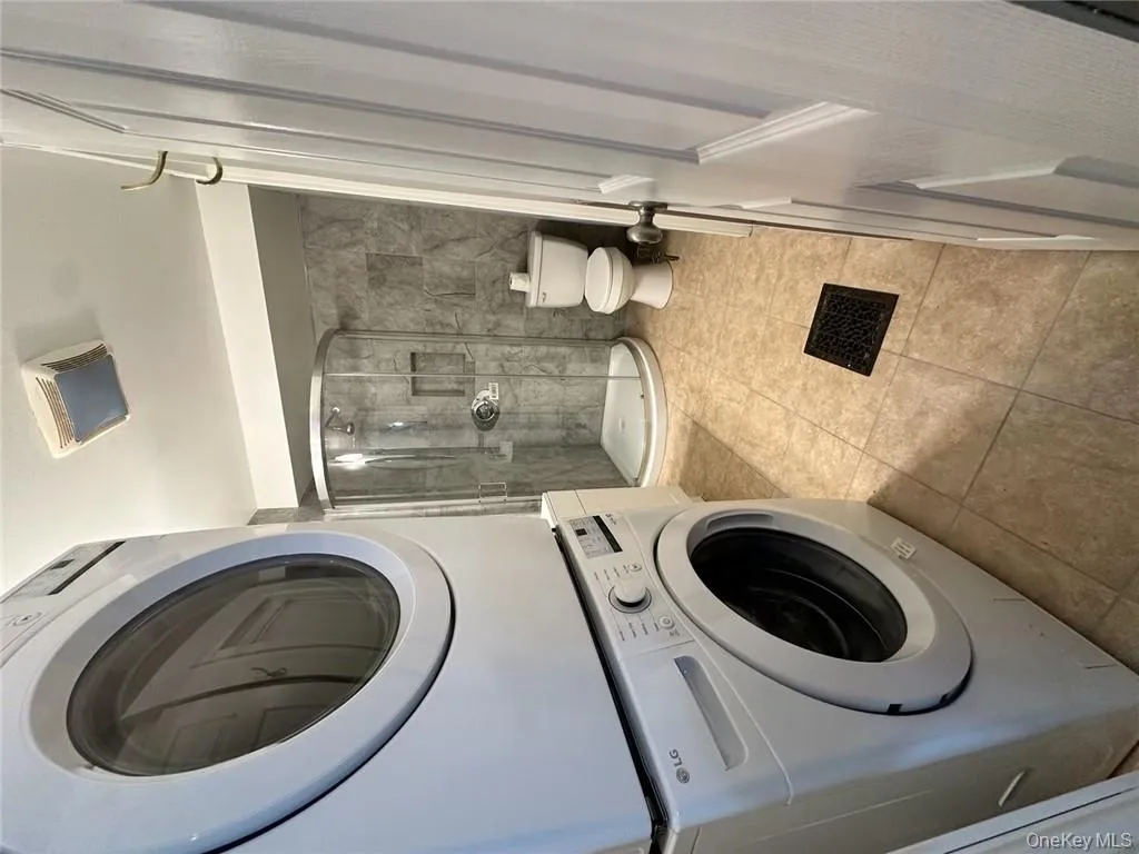 Laundry area featuring tile walls, stacked washer / drying machine, and light tile patterned flooring Laundry area featuring tile walls, stacked washer / drying machine, and light tile patterned flooring