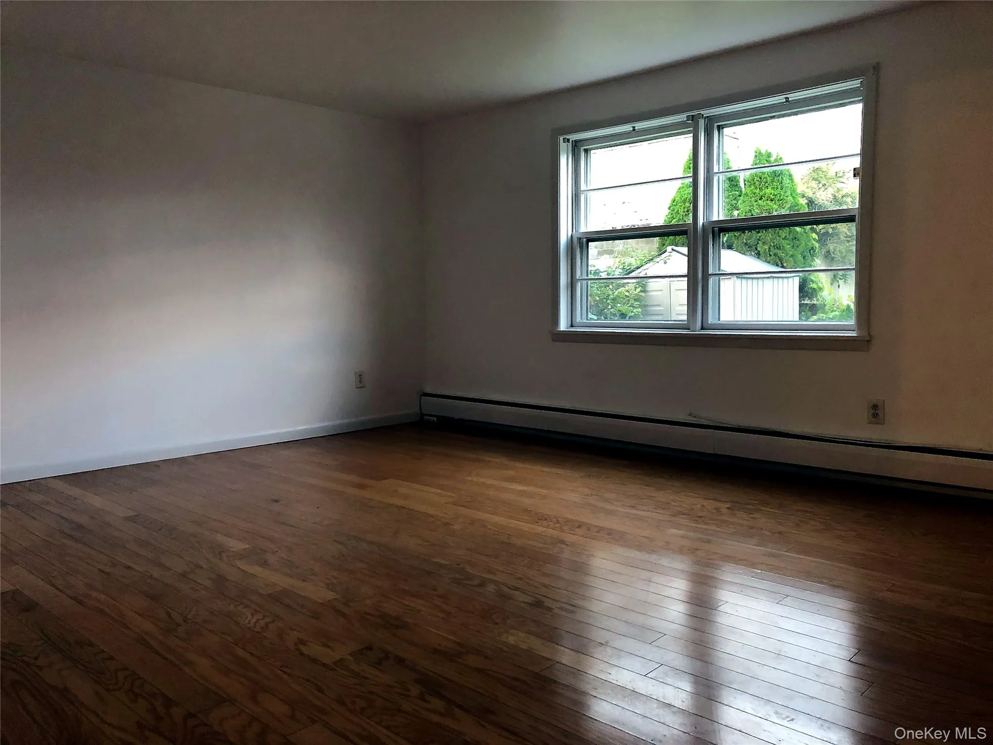 Unfurnished room featuring a baseboard heating unit and dark wood-style flooring Unfurnished room featuring a baseboard heating unit and dark wood-style flooring
