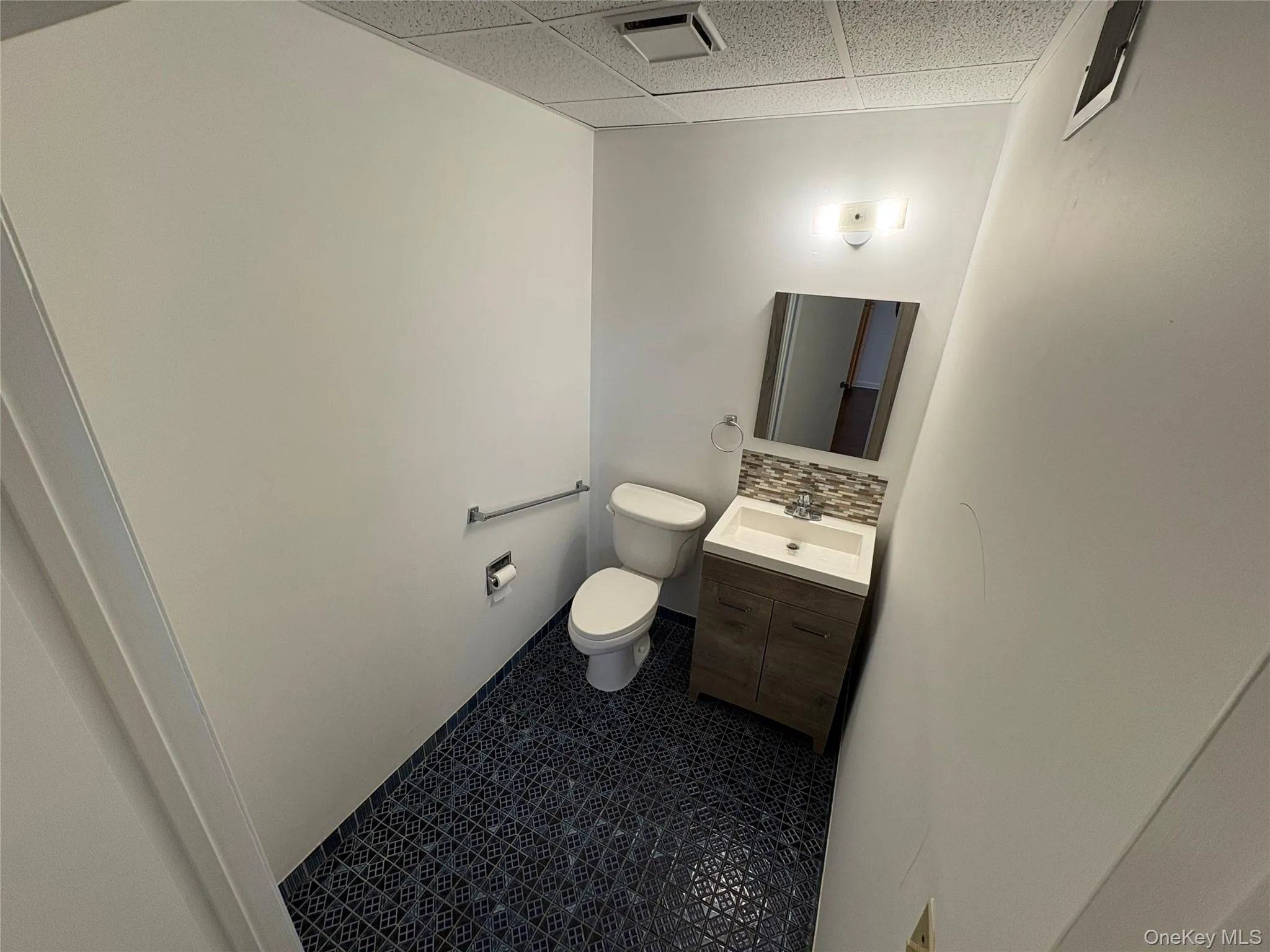 Bathroom featuring a drop ceiling, vanity, backsplash, and dark tile patterned floors Bathroom featuring a drop ceiling, vanity, backsplash, and dark tile patterned floors