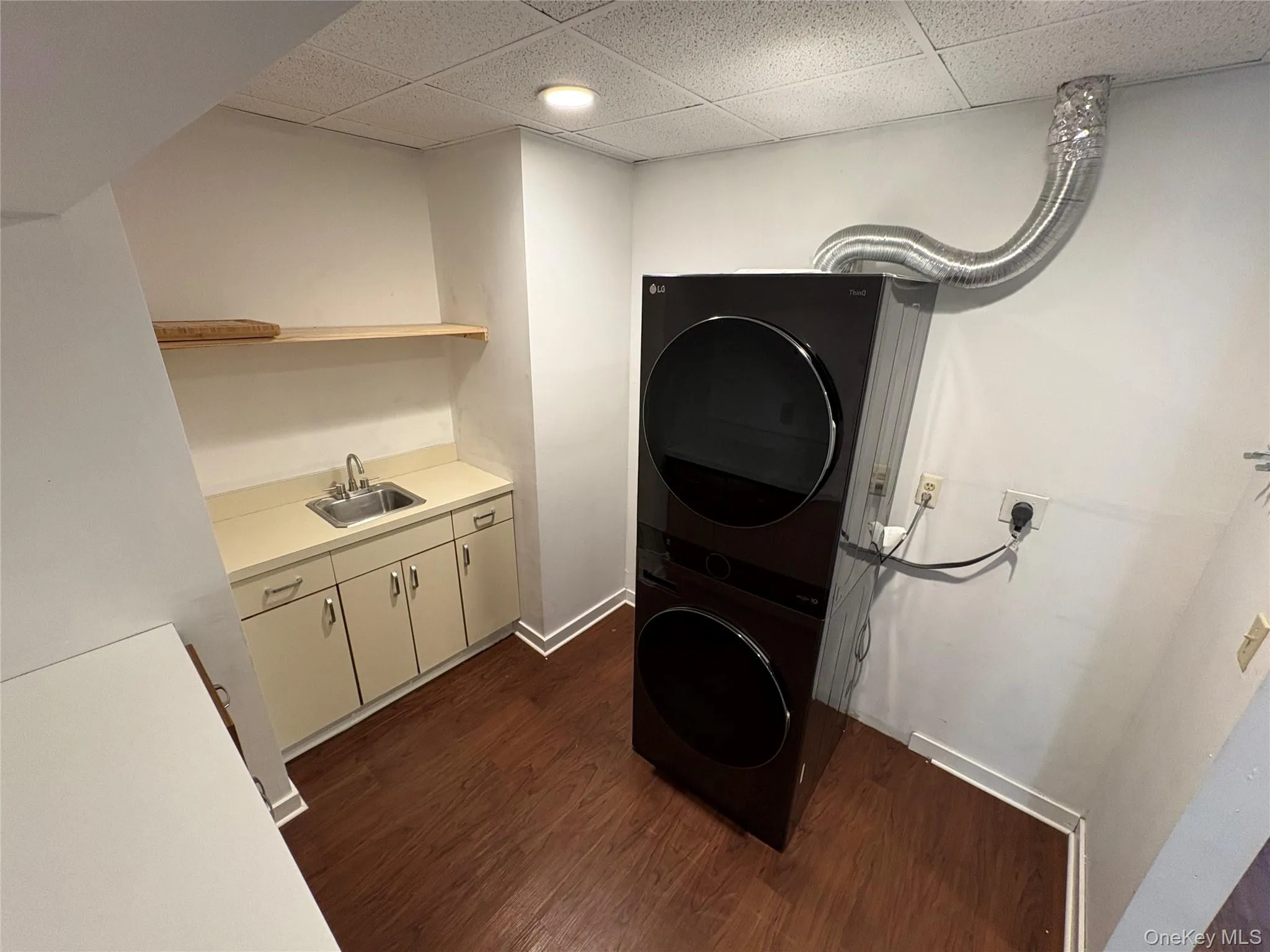 Laundry room with dark wood finished floors, a drop ceiling, and stacked washer / drying machine Laundry room with dark wood finished floors, a drop ceiling, and stacked washer / drying machine