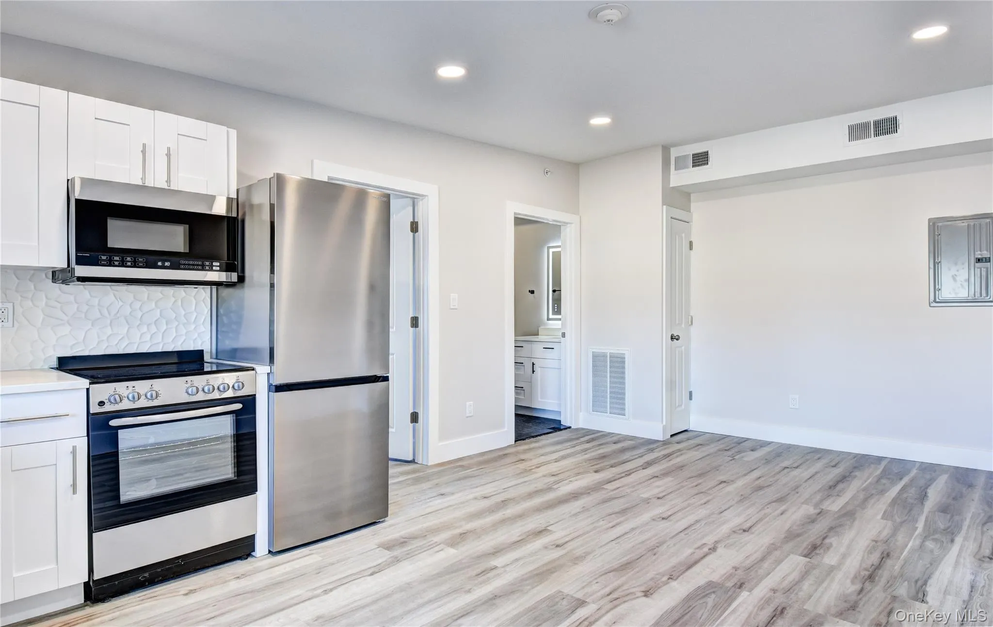 Kitchen featuring stainless steel appliances, white cabinetry, backsplash, recessed lighting, and light wood finished floors Kitchen featuring stainless steel appliances, white cabinetry, backsplash, recessed lighting, and light wood finished floors