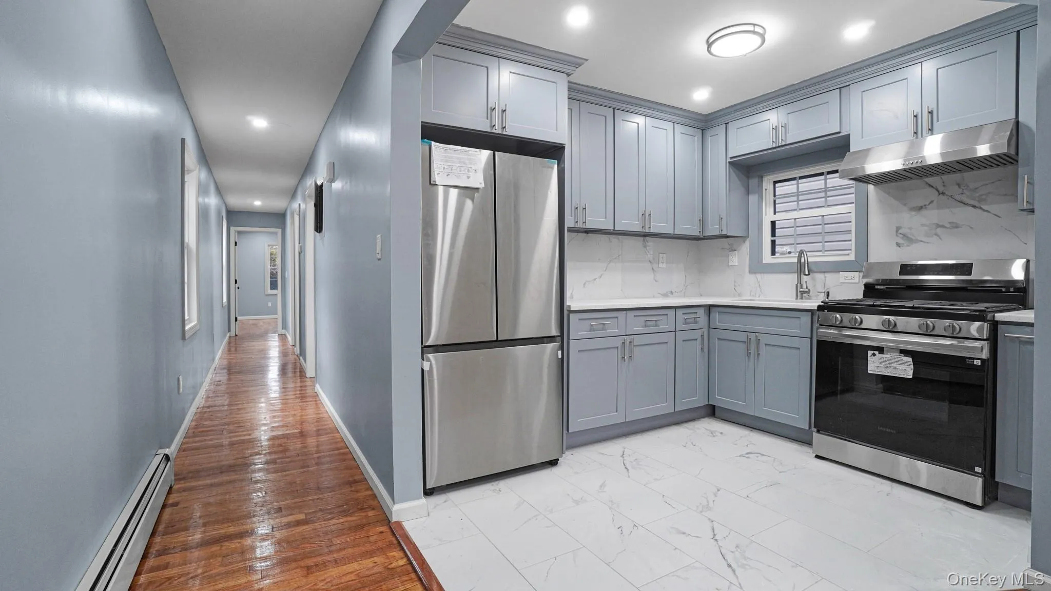 Kitchen featuring stainless steel appliances, a baseboard heating unit, gray cabinets, under cabinet range hood, and backsplash Kitchen featuring stainless steel appliances, a baseboard heating unit, gray cabinets, under cabinet range hood, and backsplash
