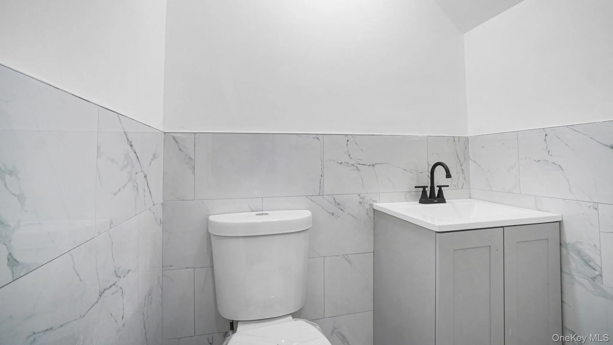 Bathroom featuring tile walls, vanity, and wainscoting Bathroom featuring tile walls, vanity, and wainscoting