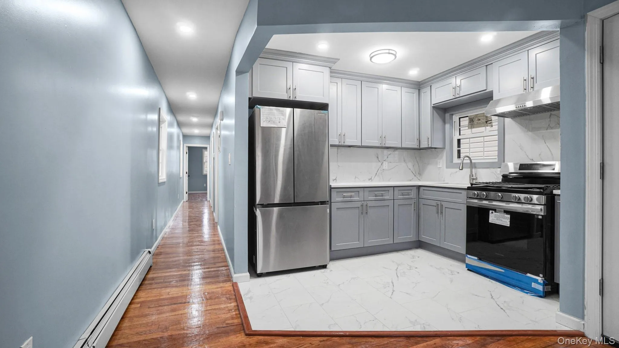 Kitchen with appliances with stainless steel finishes, a baseboard radiator, light marble finish floors, backsplash, and gray cabinetry Kitchen with appliances with stainless steel finishes, a baseboard radiator, light marble finish floors, backsplash, and gray cabinetry