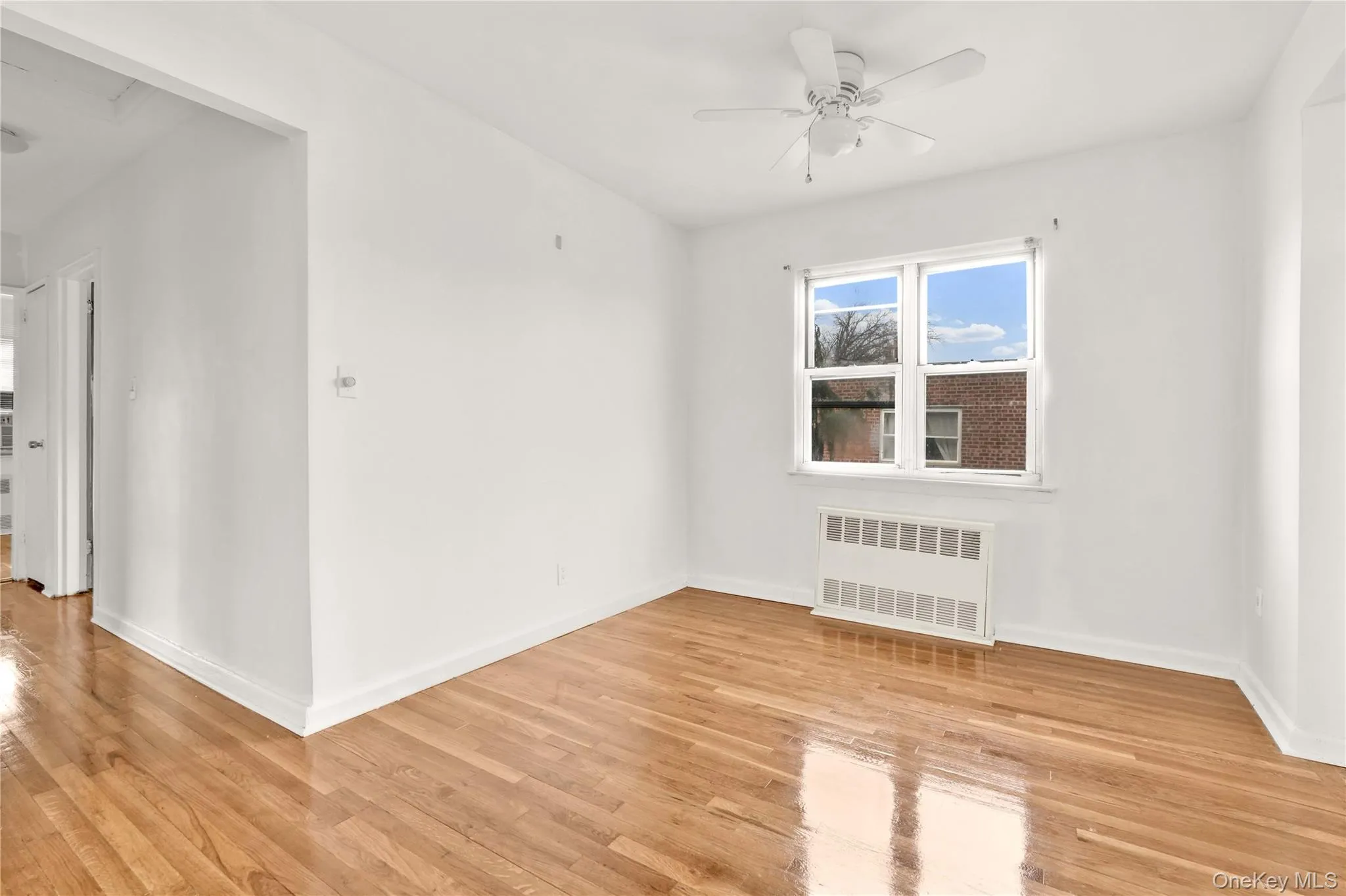 Empty room featuring radiator heating unit, light wood-style flooring, ceiling fan, and attic access Empty room featuring radiator heating unit, light wood-style flooring, ceiling fan, and attic access