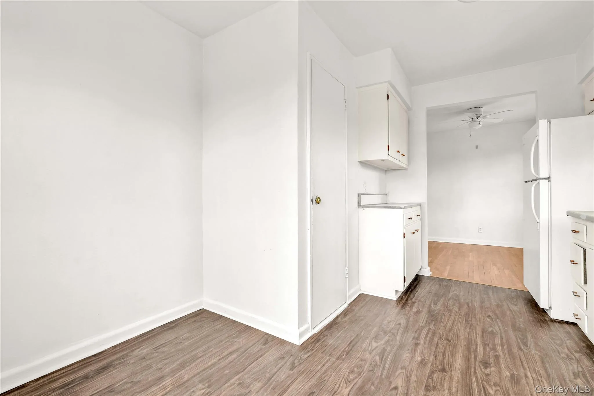 Kitchen with white cabinetry, freestanding refrigerator, dark wood-type flooring, light countertops, and a ceiling fan Kitchen with white cabinetry, freestanding refrigerator, dark wood-type flooring, light countertops, and a ceiling fan