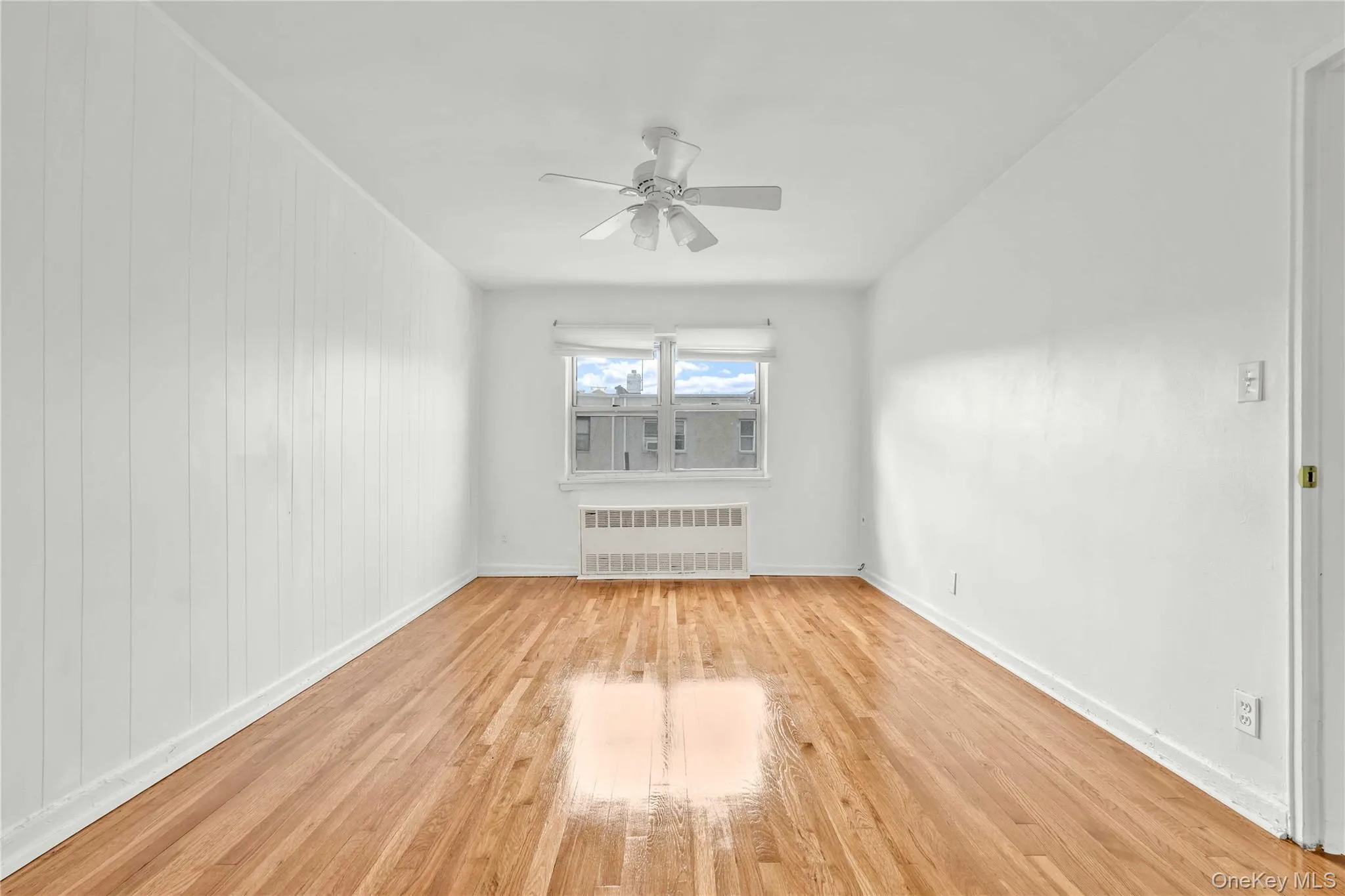 Unfurnished room with radiator, light wood-type flooring, and a ceiling fan Unfurnished room with radiator, light wood-type flooring, and a ceiling fan