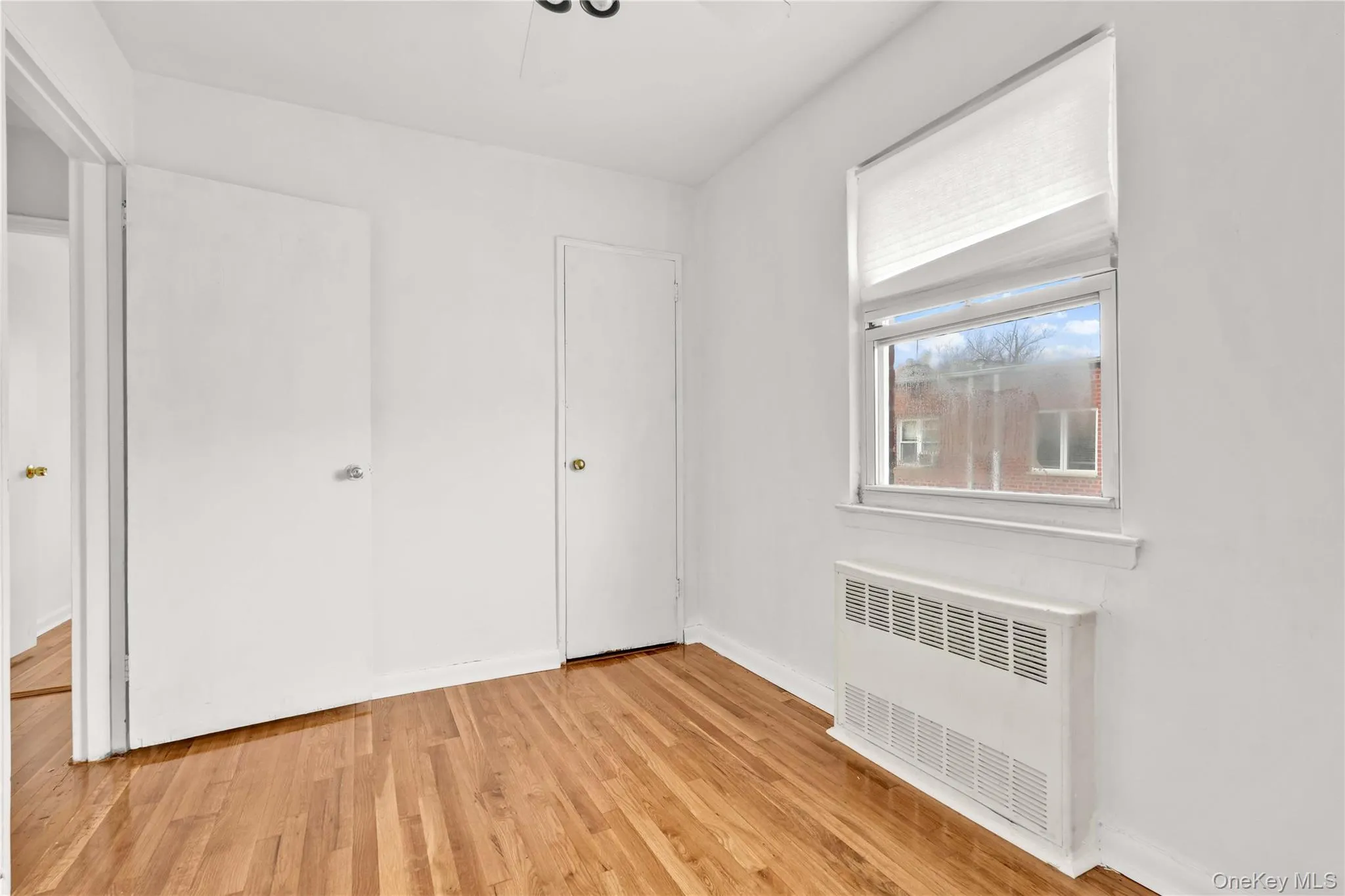 Unfurnished bedroom with radiator heating unit, light wood-style floors, and a ceiling fan Unfurnished bedroom with radiator heating unit, light wood-style floors, and a ceiling fan