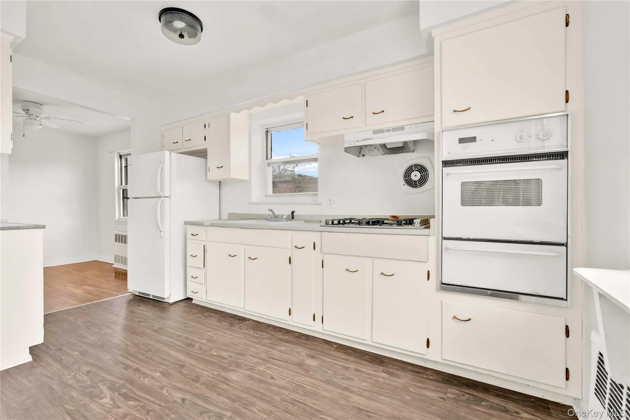 Kitchen featuring light wood finished floors, white appliances, a warming drawer, light countertops, and white cabinetry Kitchen featuring light wood finished floors, white appliances, a warming drawer, light countertops, and white cabinetry