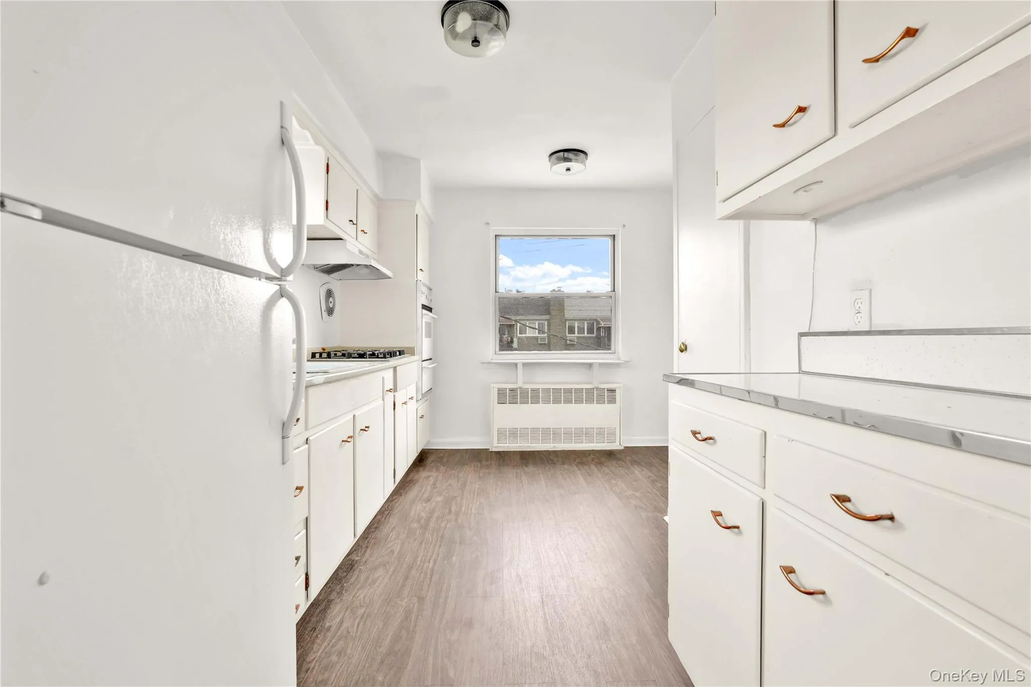 Kitchen featuring freestanding refrigerator, white cabinets, dark wood finished floors, and radiator Kitchen featuring freestanding refrigerator, white cabinets, dark wood finished floors, and radiator