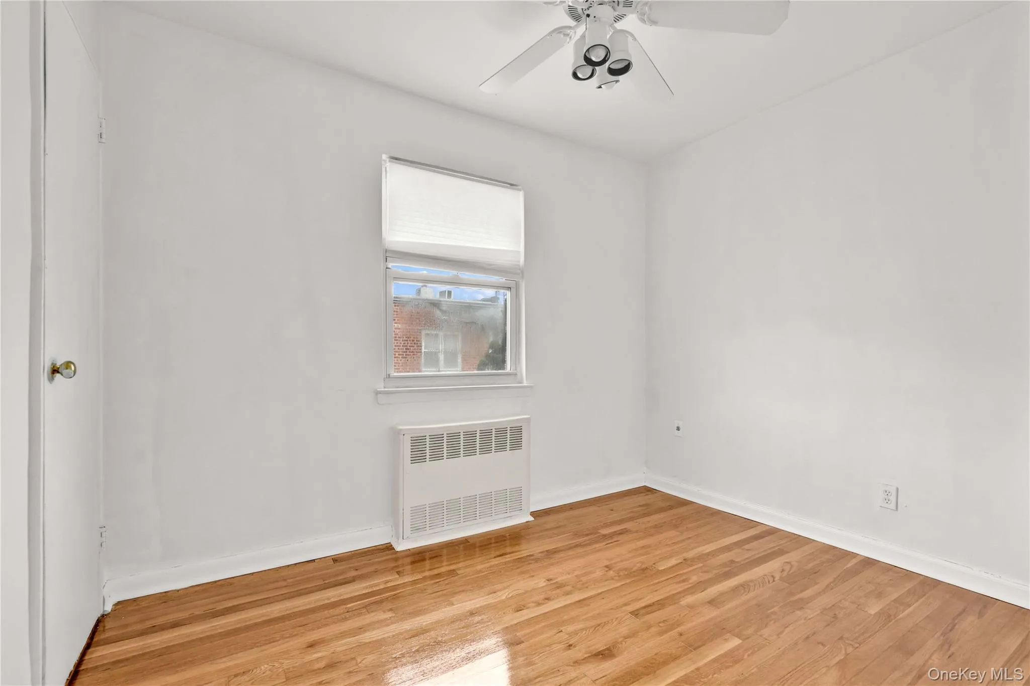 Empty room with radiator, wood finished floors, and ceiling fan Empty room with radiator, wood finished floors, and ceiling fan