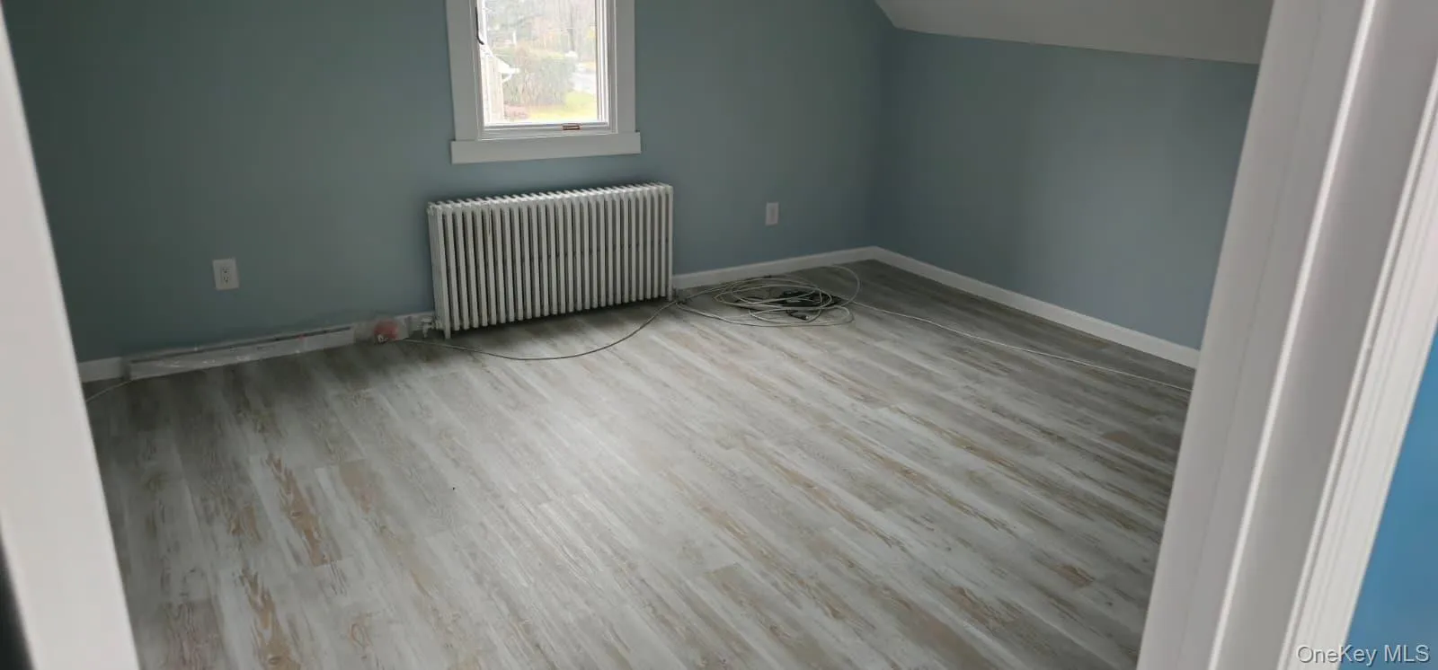 Additional living space featuring radiator, light wood-style floors, lofted ceiling, and a baseboard radiator Additional living space featuring radiator, light wood-style floors, lofted ceiling, and a baseboard radiator