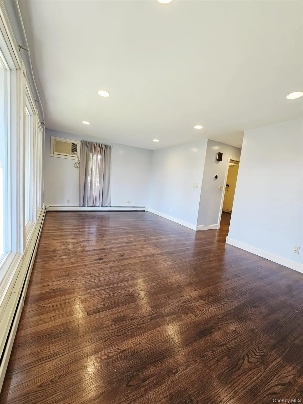 Unfurnished room featuring a baseboard radiator, recessed lighting, dark wood-type flooring, and a wall unit AC Unfurnished room featuring a baseboard radiator, recessed lighting, dark wood-type flooring, and a wall unit AC