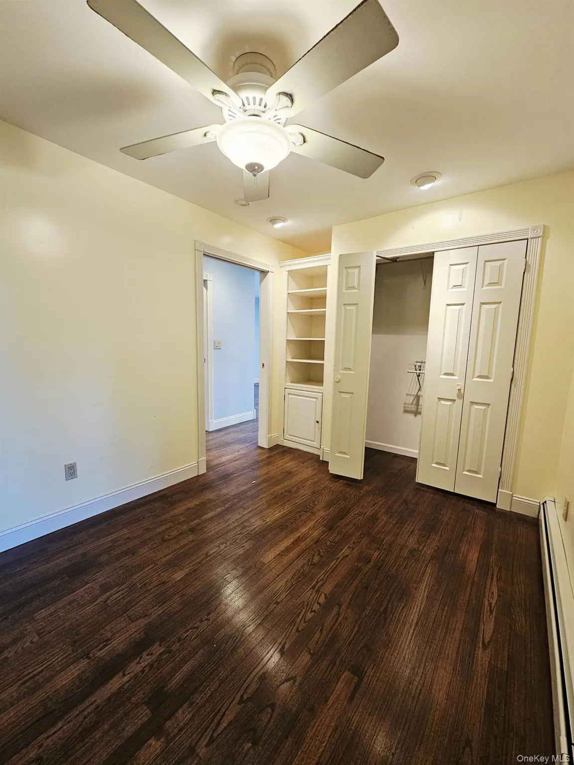 Unfurnished bedroom featuring a baseboard radiator, dark wood-style floors, a closet, and a ceiling fan Unfurnished bedroom featuring a baseboard radiator, dark wood-style floors, a closet, and a ceiling fan