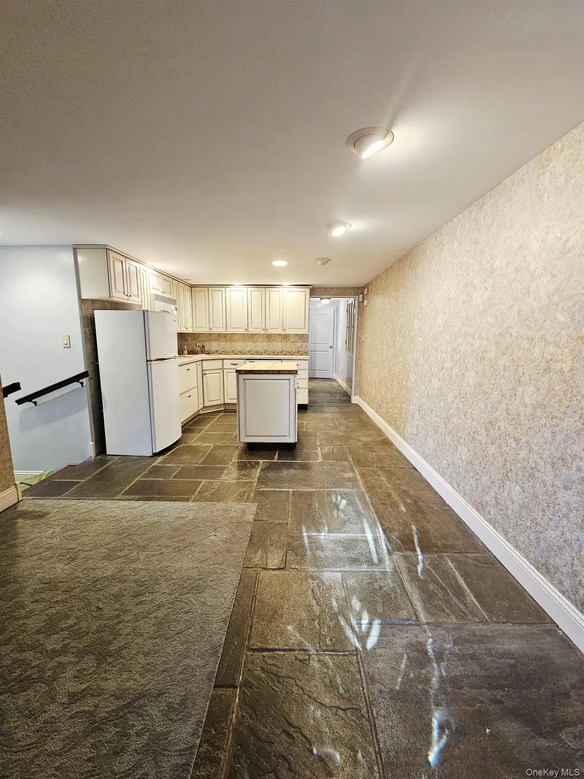 Kitchen with freestanding refrigerator, wallpapered walls, light countertops, a kitchen island, and stone tile floors Kitchen with freestanding refrigerator, wallpapered walls, light countertops, a kitchen island, and stone tile floors