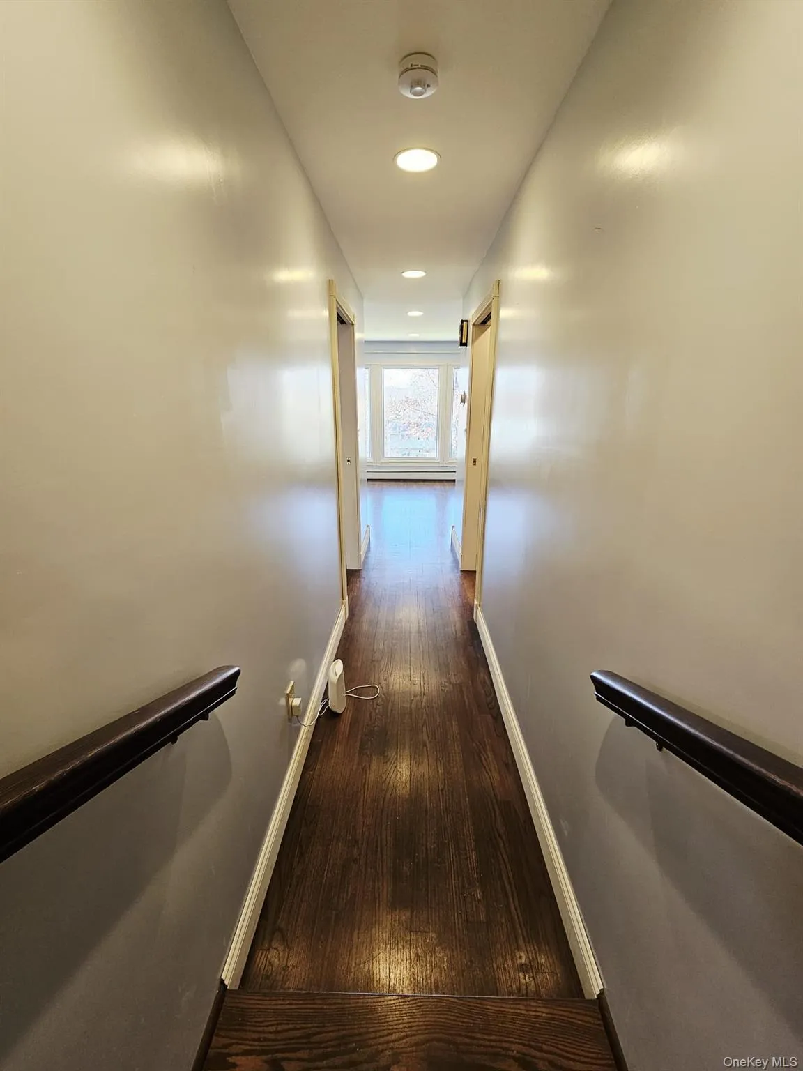 Corridor with dark wood-type flooring, recessed lighting, and a baseboard heating unit Corridor with dark wood-type flooring, recessed lighting, and a baseboard heating unit