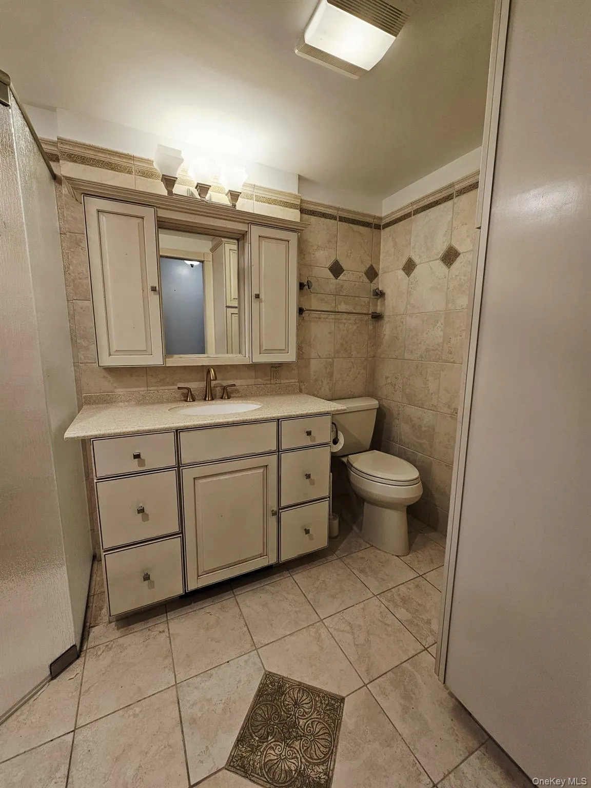 Full bath featuring vanity, tile walls, and light tile patterned floors Full bath featuring vanity, tile walls, and light tile patterned floors