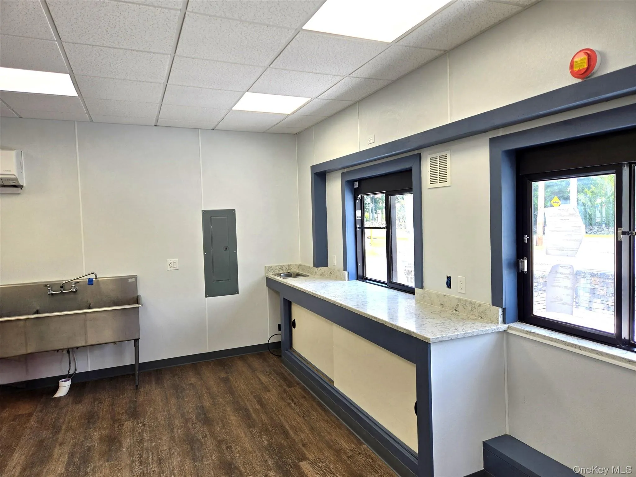 Kitchen featuring a drop ceiling, electric panel, dark wood-type flooring, an AC wall unit, and light stone countertops Kitchen featuring a drop ceiling, electric panel, dark wood-type flooring, an AC wall unit, and light stone countertops