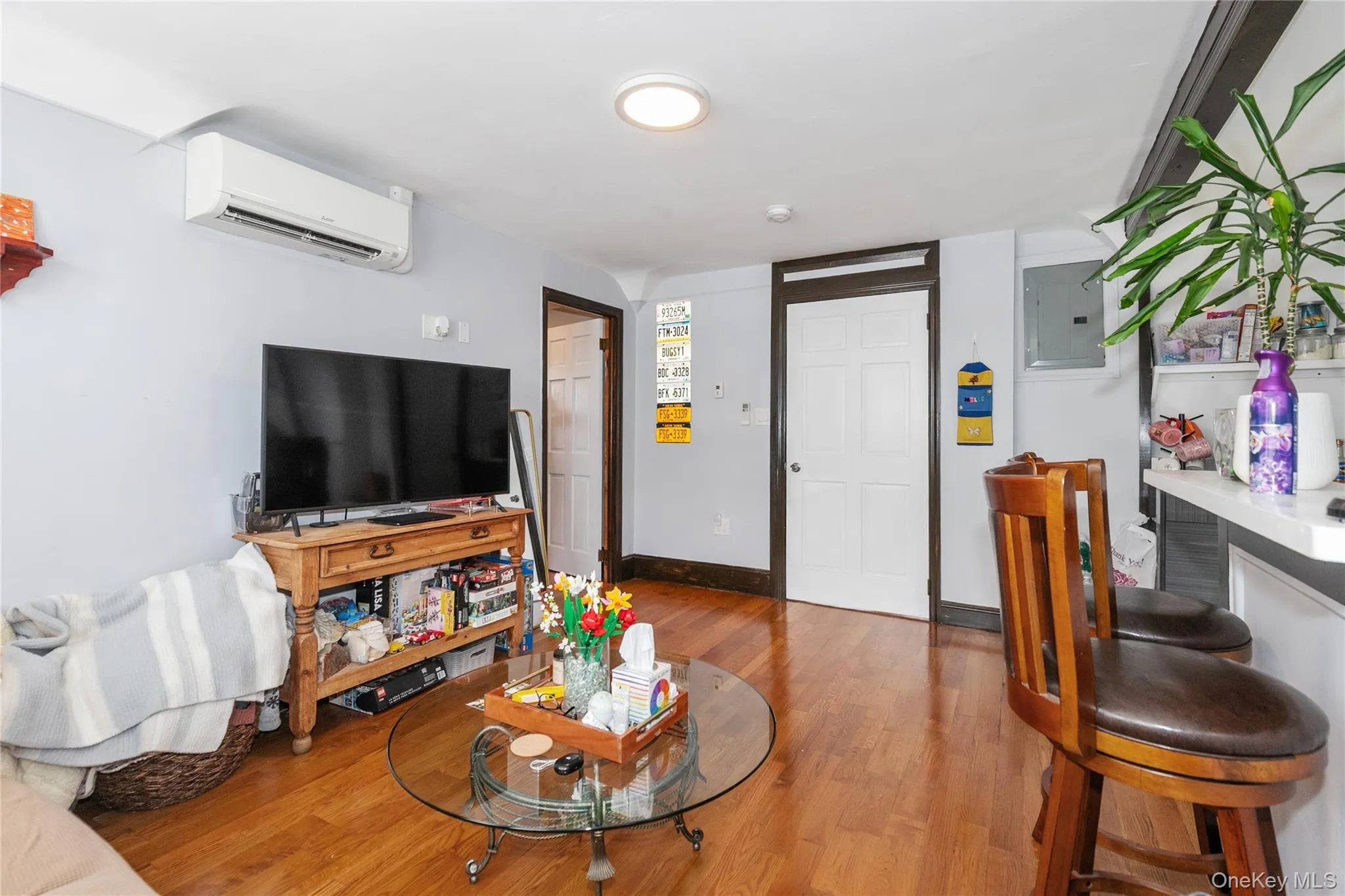Living area with electric panel, a wall mounted AC, and wood finished floors Living area with electric panel, a wall mounted AC, and wood finished floors