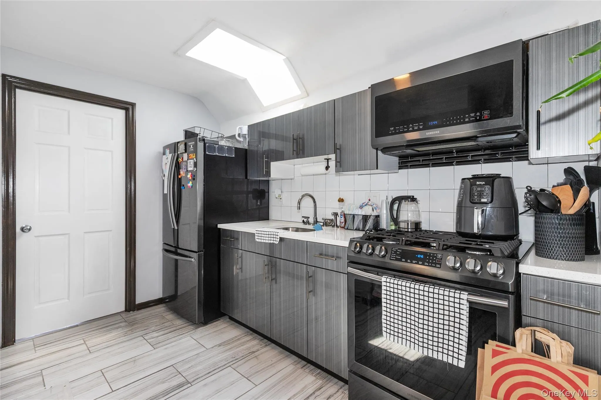 Kitchen featuring backsplash, appliances with stainless steel finishes, vaulted ceiling, gray cabinetry, and modern cabinets Kitchen featuring backsplash, appliances with stainless steel finishes, vaulted ceiling, gray cabinetry, and modern cabinets