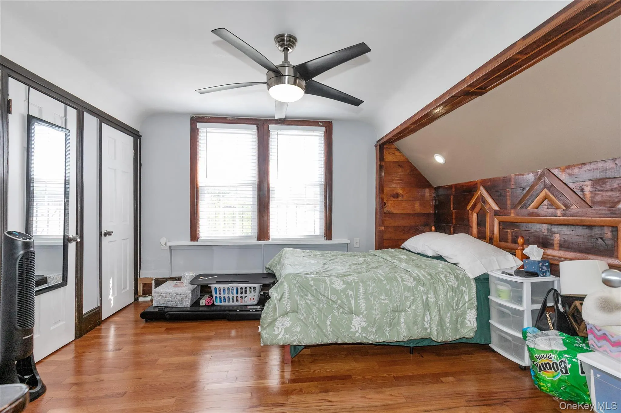 Bedroom with wooden walls, lofted ceiling, wood finished floors, a ceiling fan, and an accent wall Bedroom with wooden walls, lofted ceiling, wood finished floors, a ceiling fan, and an accent wall