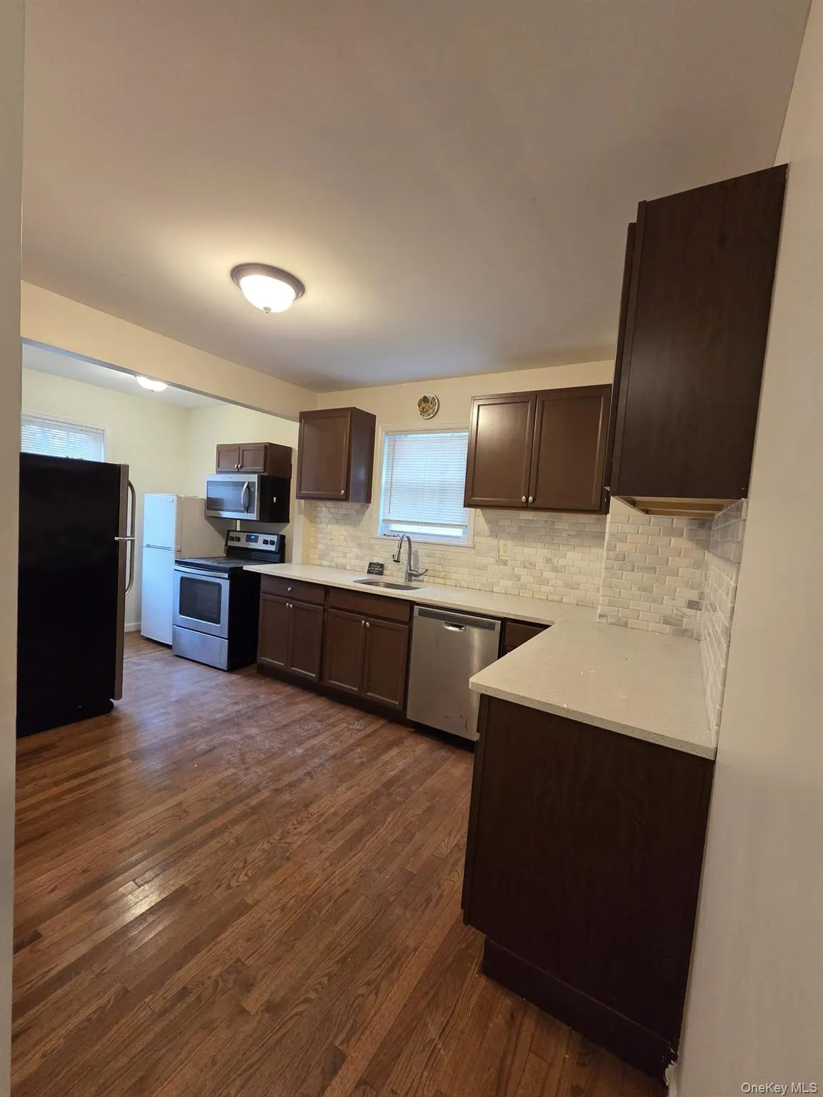 Kitchen featuring dark brown cabinetry, appliances with stainless steel finishes, backsplash, and dark wood finished floors Kitchen featuring dark brown cabinetry, appliances with stainless steel finishes, backsplash, and dark wood finished floors