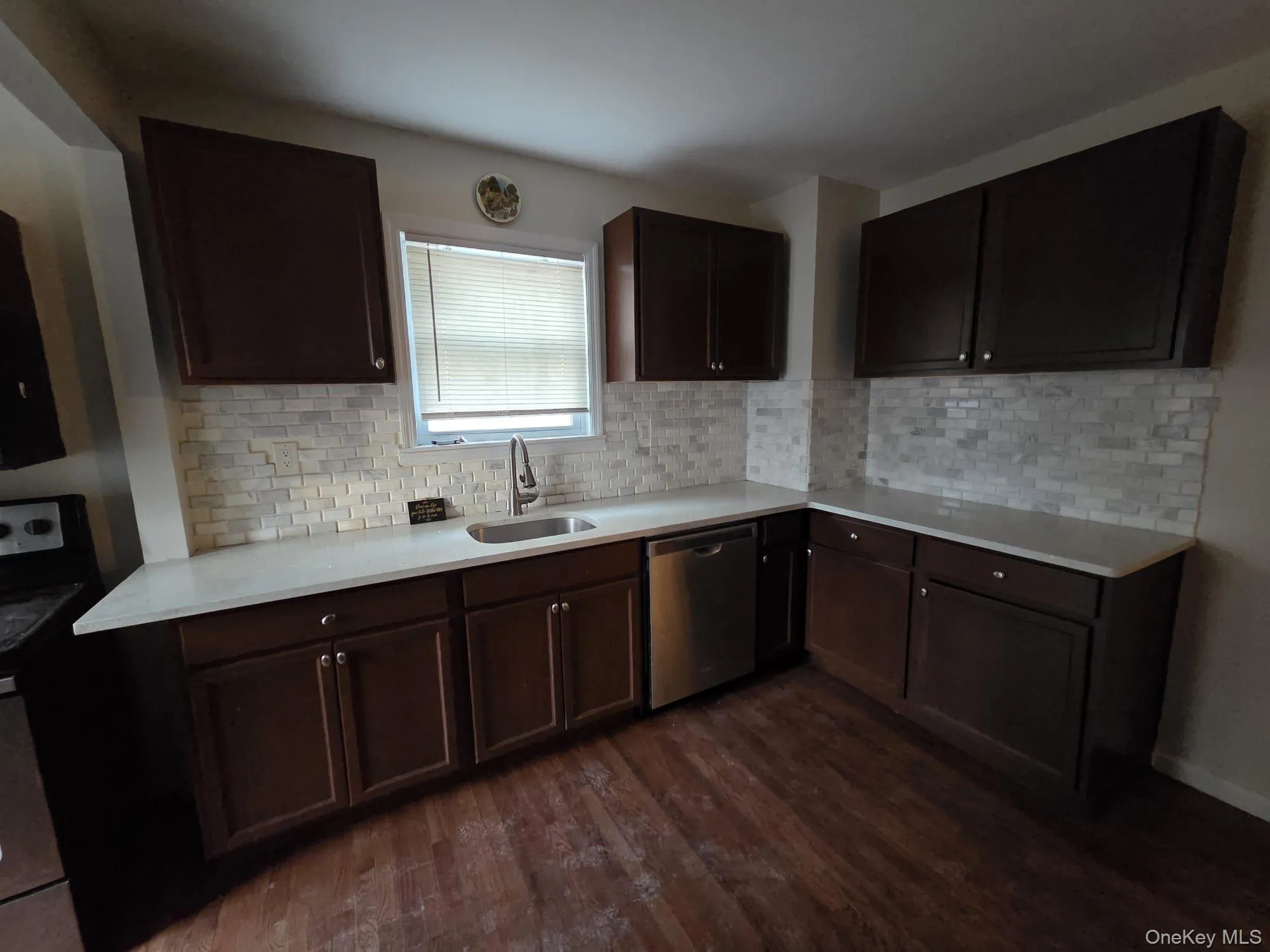 Kitchen with dark brown cabinets, black electric range oven, stainless steel dishwasher, decorative backsplash, and dark wood finished floors Kitchen with dark brown cabinets, black electric range oven, stainless steel dishwasher, decorative backsplash, and dark wood finished floors