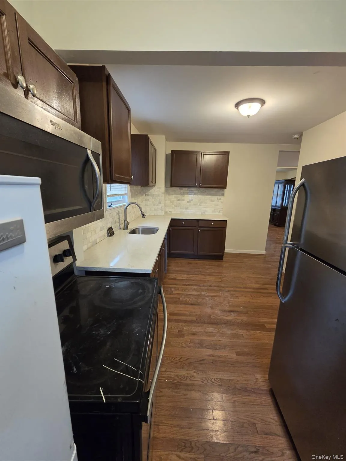Kitchen featuring dark brown cabinets, appliances with stainless steel finishes, decorative backsplash, dark wood finished floors, and light stone counters Kitchen featuring dark brown cabinets, appliances with stainless steel finishes, decorative backsplash, dark wood finished floors, and light stone counters